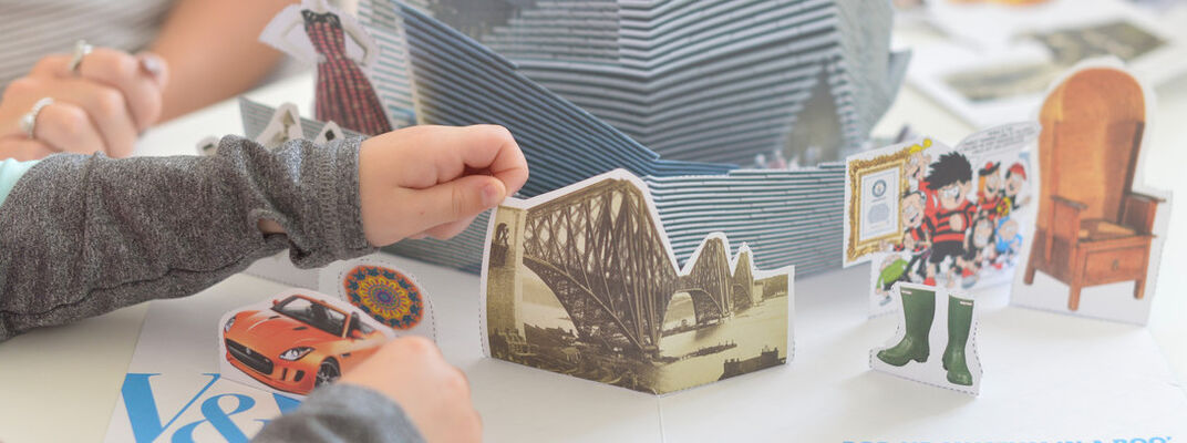 A photo of a child creating a pop up museum in a book using paper cut outs of objects in the museum