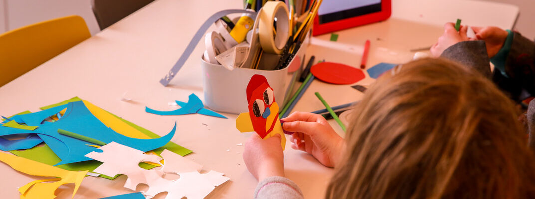 A photo of a child making a character out of pieces of coloured paper