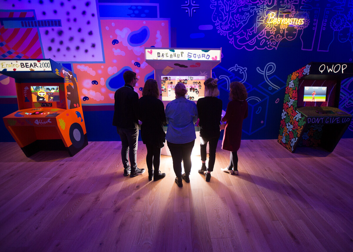 A group of people standing around an arcade machine at V&A Dundee