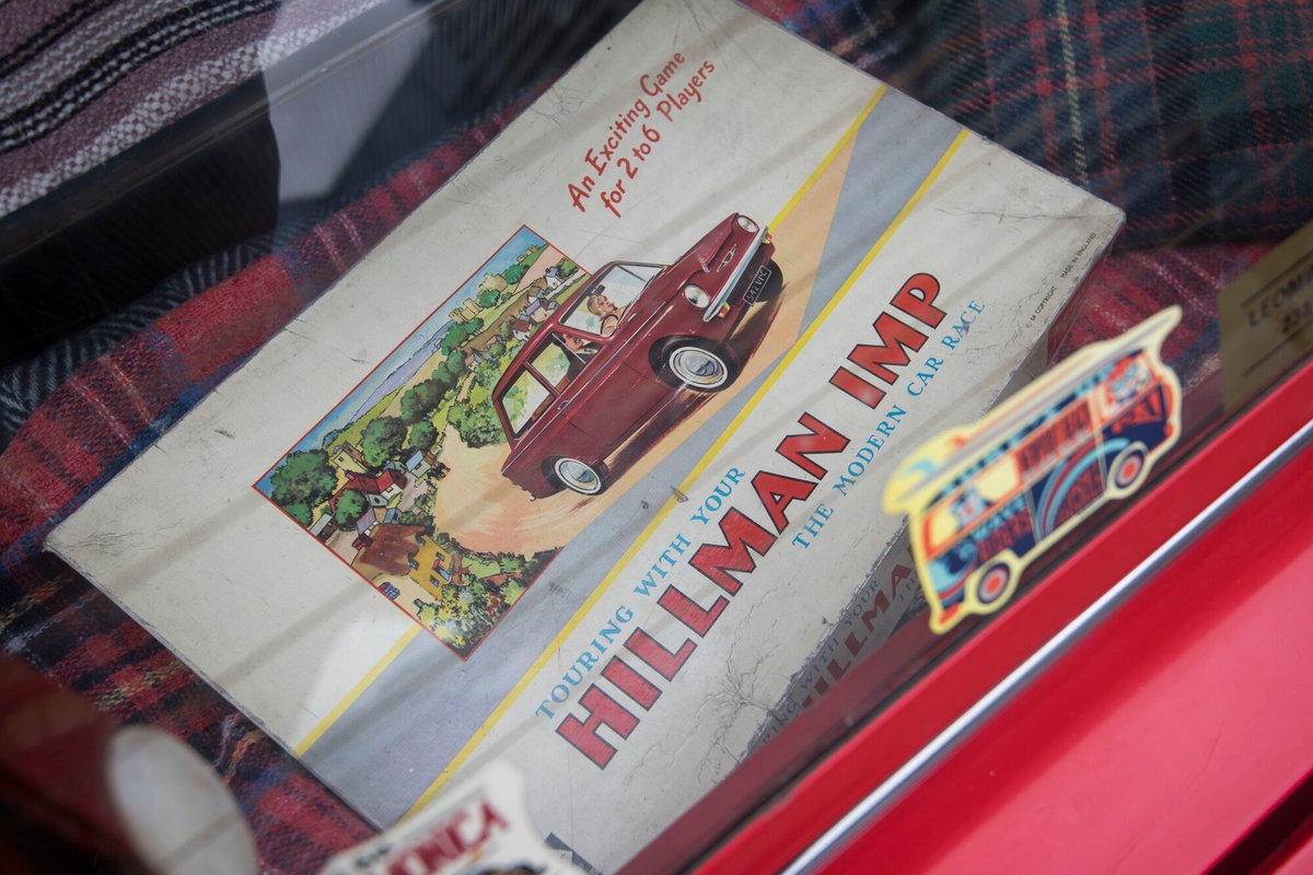 A board game box lying in the back of a red car. the box has a car on it and a vintage look