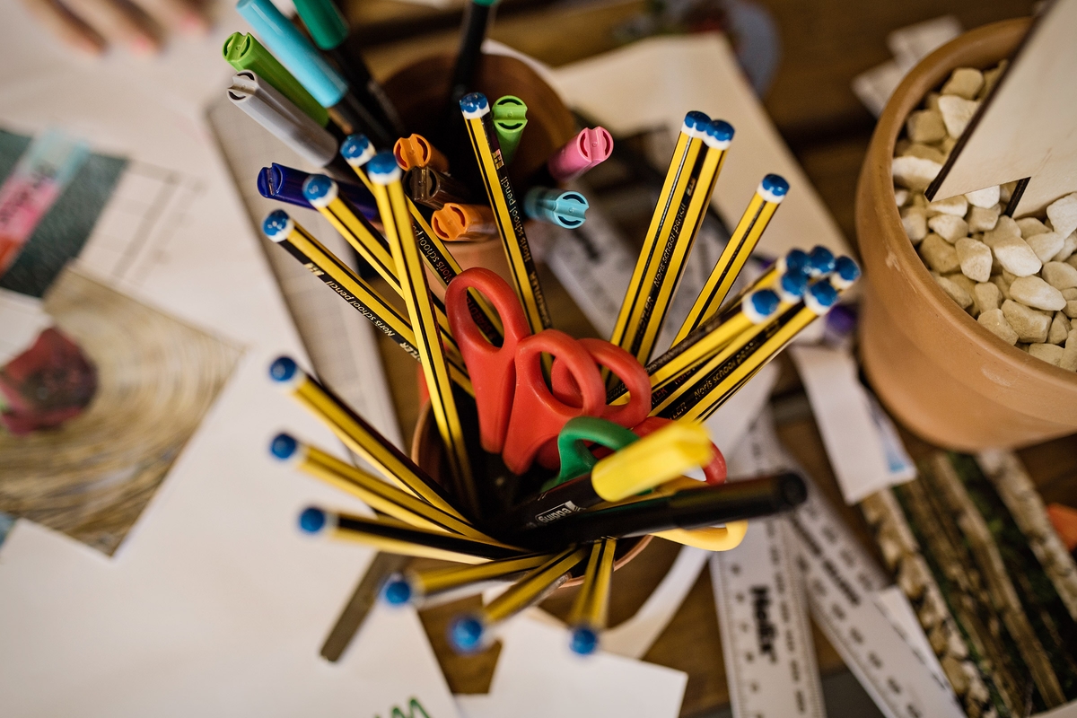 A Birds Eye view of a desk with paper across it and a pot of pencils.