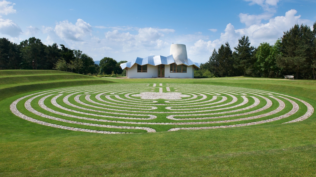 Maggie's Centre Dundee, designed by Frank Gehry, is a white building with a zigzag shiny metal roof, with a spiral path garden in front.
