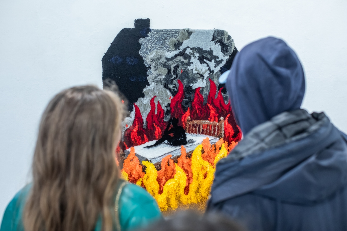 Image of people looking at a tapestry depicting a black figure in a bed surrounded by flames