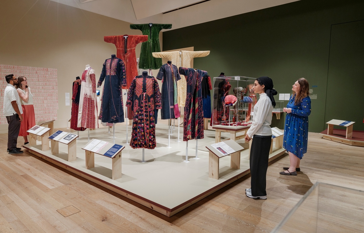 Visitors observe an exhibit of traditional, colourful garments displayed on mannequins in a museum setting.