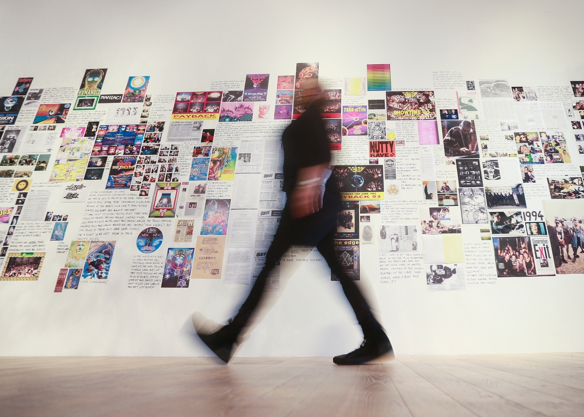 A blurred silhouette walking in front of a range of posters and stories
