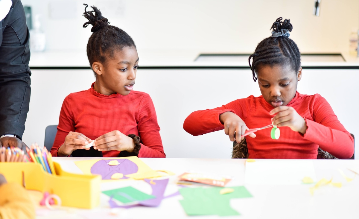 Two children sitting at a table cutting paper and making crafts.