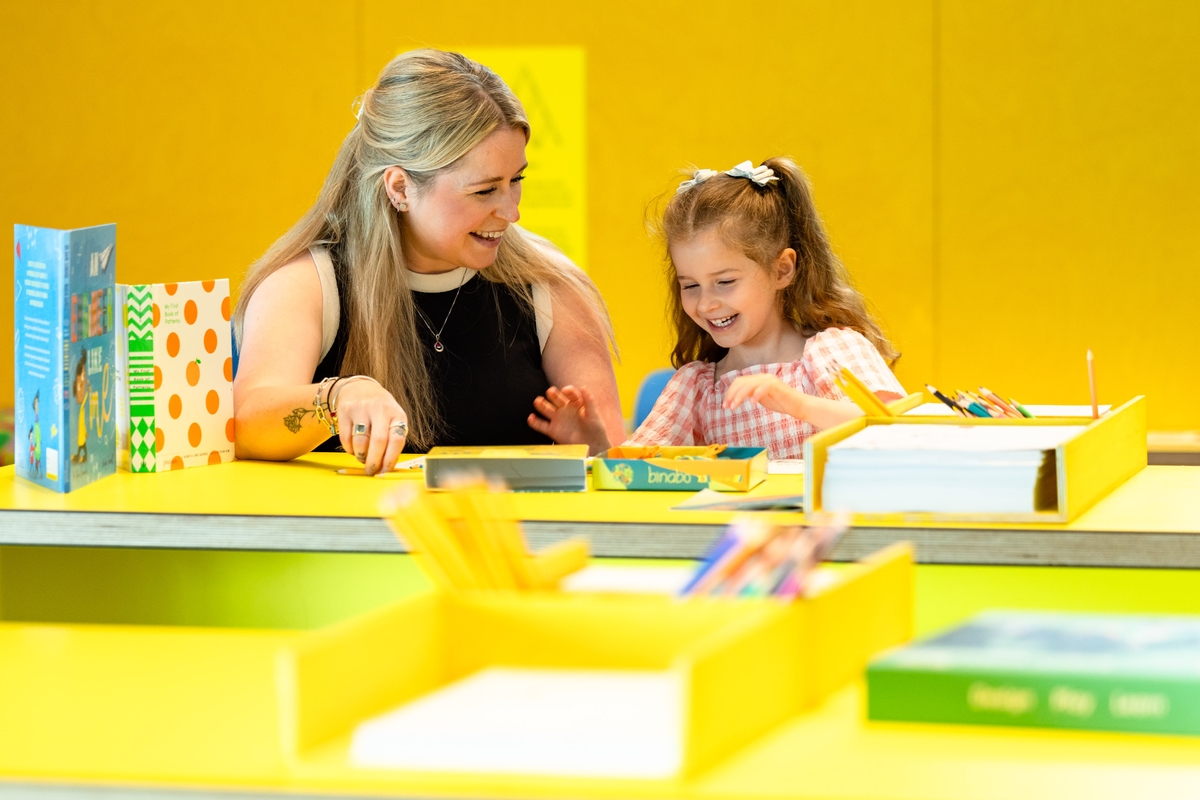 A woman and child sitting at a yellow table drawing.