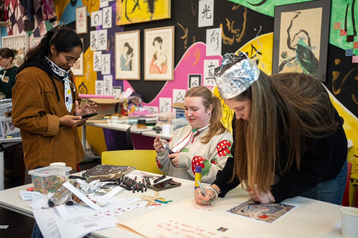 Three young women are working on a craft project in a colourful art studio
