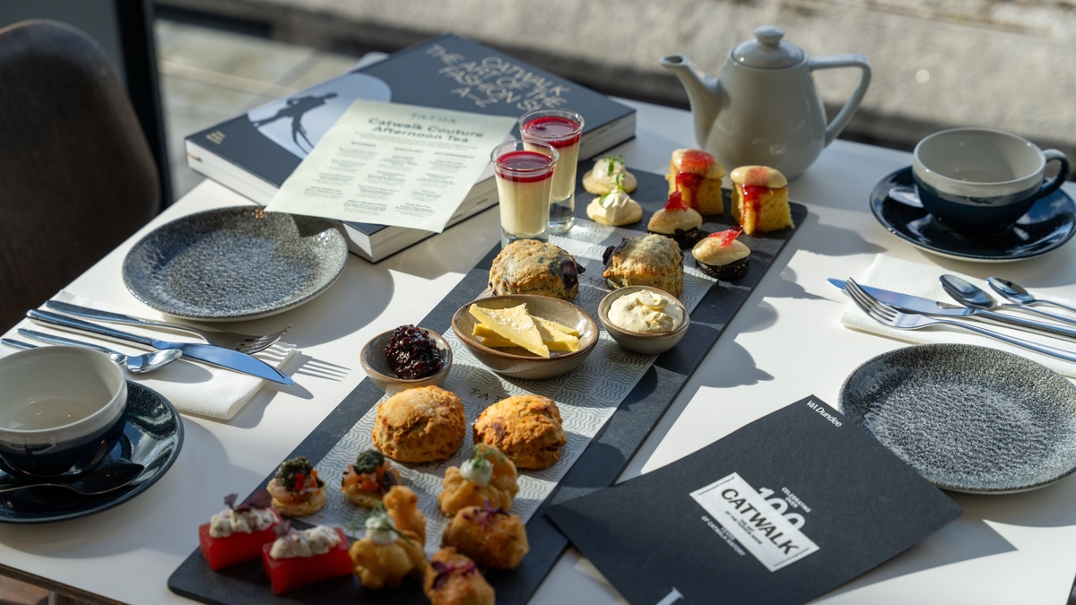 Afternoon tea spread with scones, pastries, and tea on a table, accompanied by menus and a teapot.