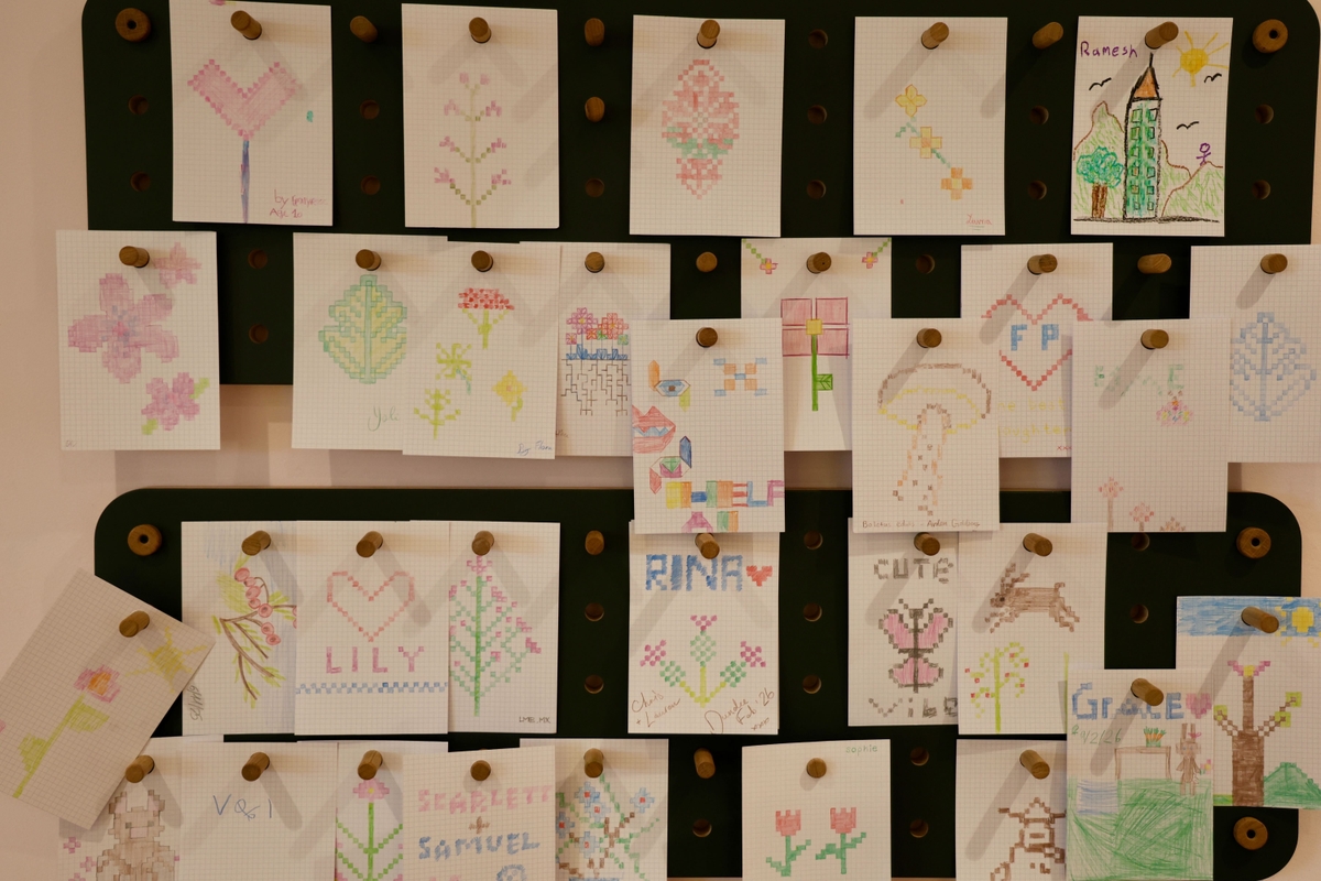 Various colourful drawings and designs pinned on a board, featuring flowers, patterns, and names like Lily and Samuel.