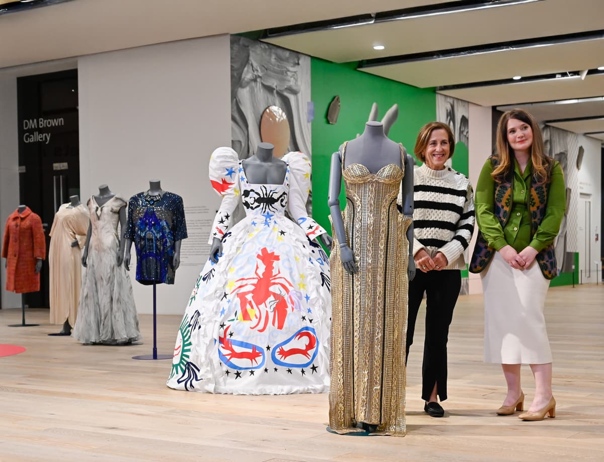 Two people posing next to mannequins.