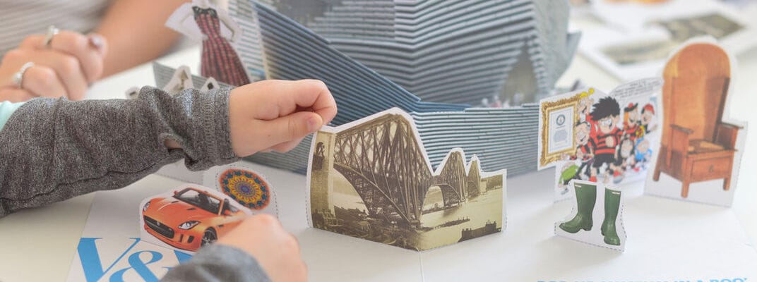 A photo of a child creating a pop up museum in a book using paper cut outs of objects in the museum