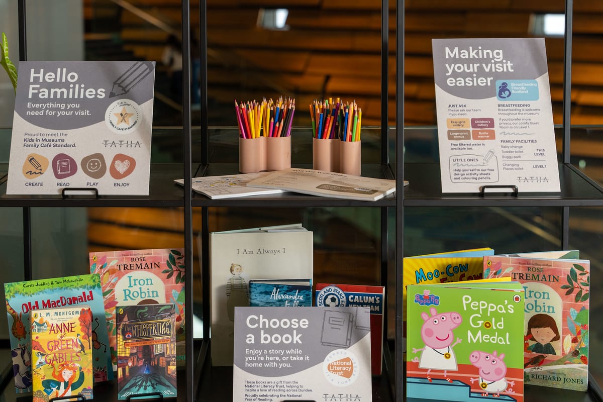 A display shelf with books, informational signs, and colorful pencils, promoting family-friendly activities and reading options.
