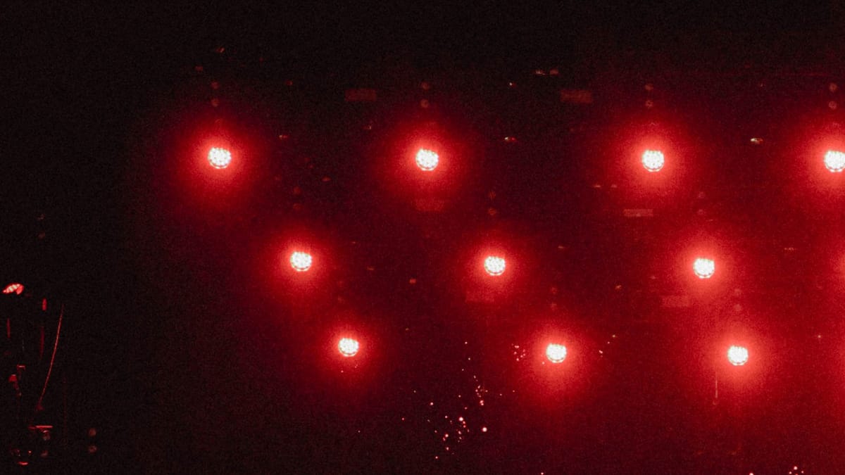 Red stage lights and a disco ball create a vivid, glowing atmosphere against a dark background.