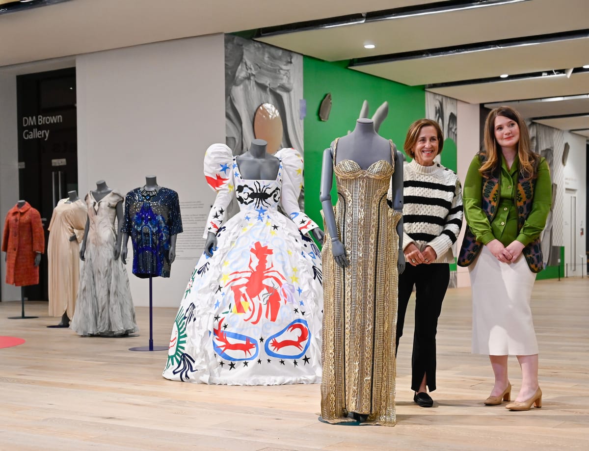 Two people posing next to mannequins.