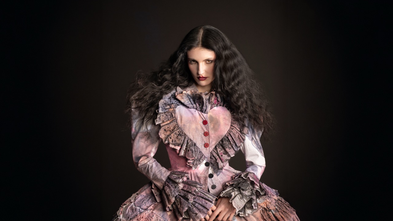 A model wearing a pink dress with a love heart detail against a black background.
