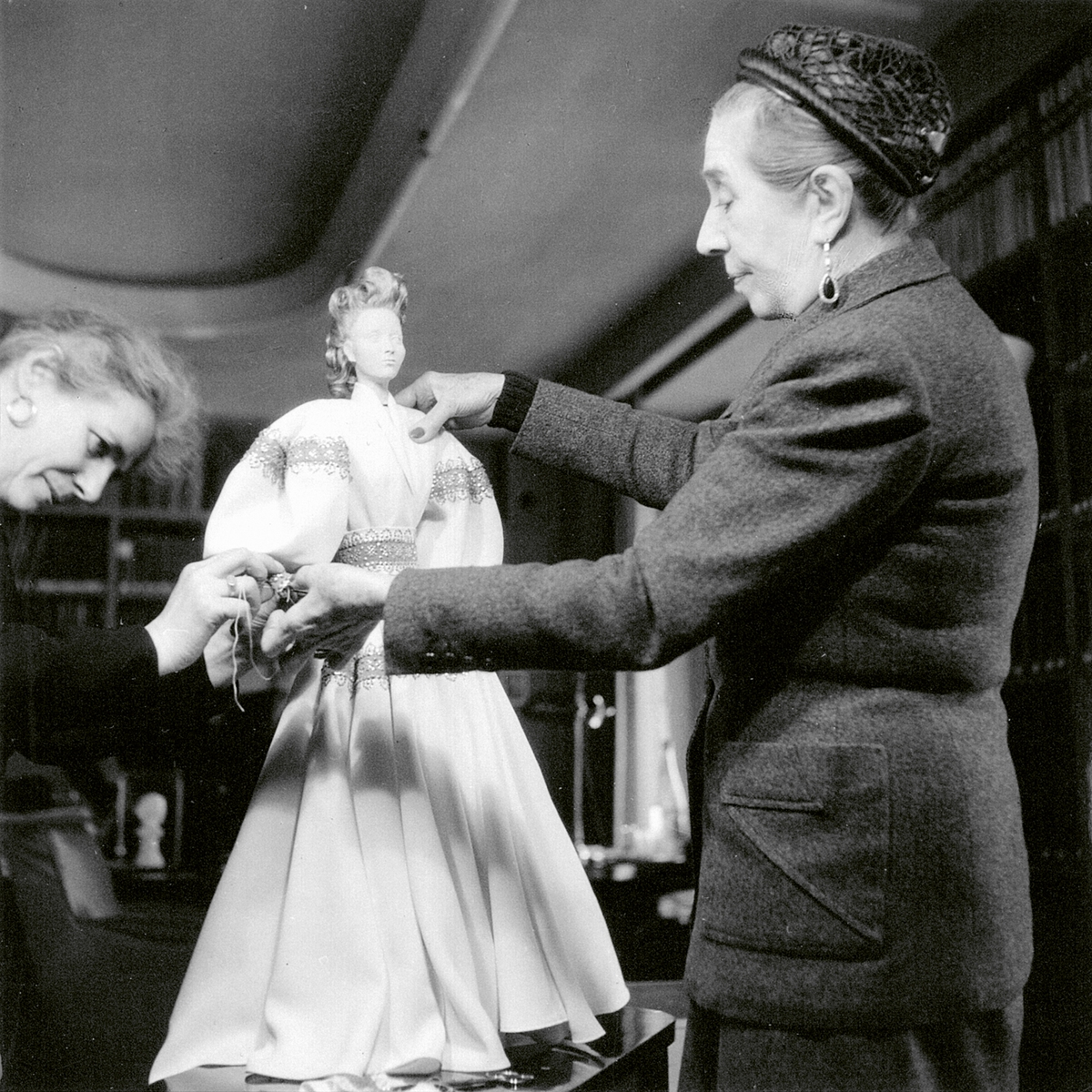 A black and white image of two women dressing a doll in a dress.