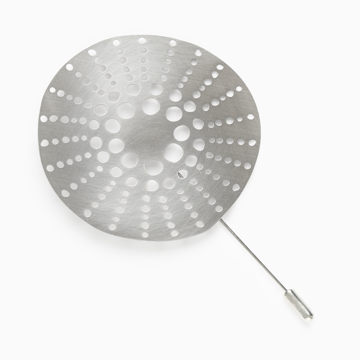 A silver brooch which is round with lots of holes pierced through the metrical in a circular design.