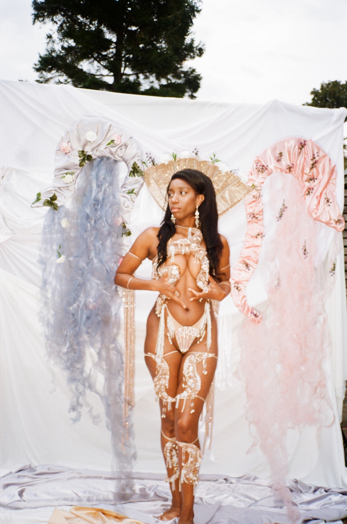 A woman wearing a gold detailed outfit standing in front of a white sheet which has pastel details coming off it.
