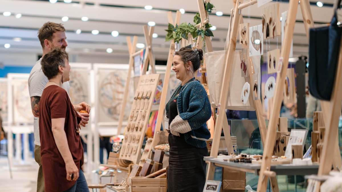 Three people standing by a wooden retail stall chatting.
