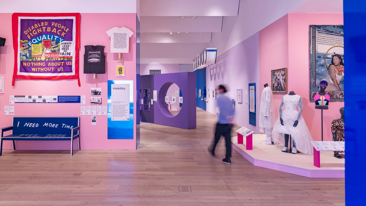 A large exhibition space, the walls are pink and purple with objects on the walls along with mannequins