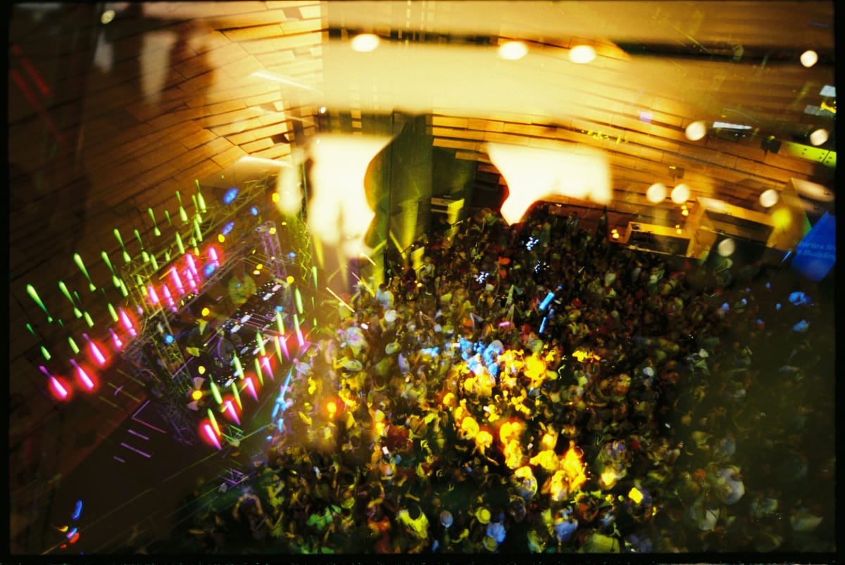 Aerial view of a vibrant, crowded party with colourful lights and energetic people dancing under a wooden ceiling.