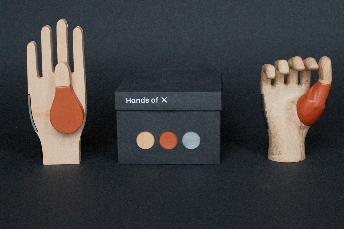 Two prosthetic hands on either side of a box which says 'hands of X'