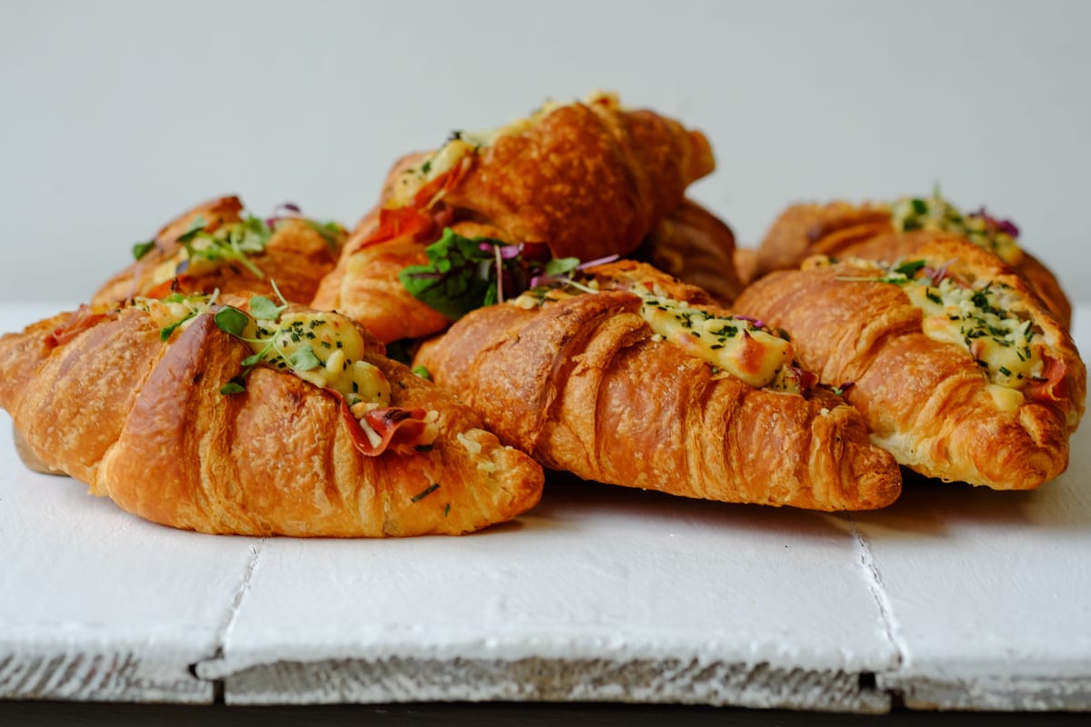 Croissants filled with melted cheese, herbs, and greens are arranged on a white wooden surface.