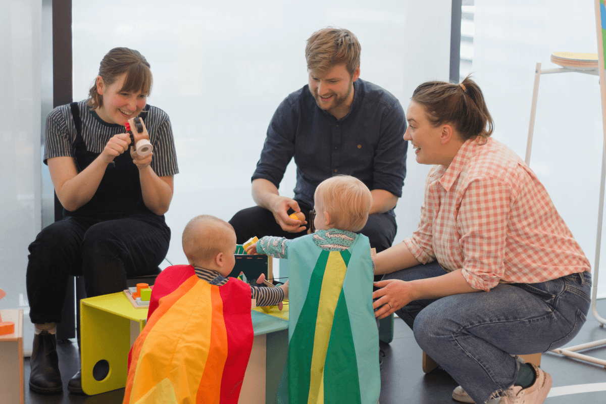 Two toddlers playing with toys with three adults
