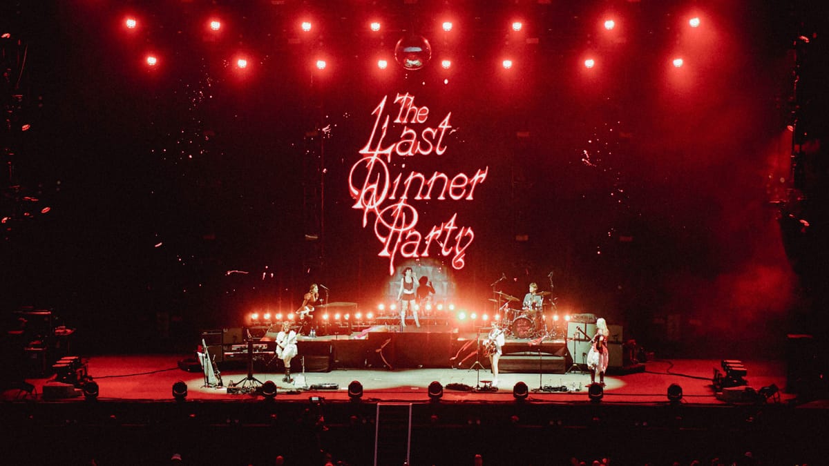 A band performs on stage under red lights, with the backdrop displaying "The Last Dinner Party" in stylized text.