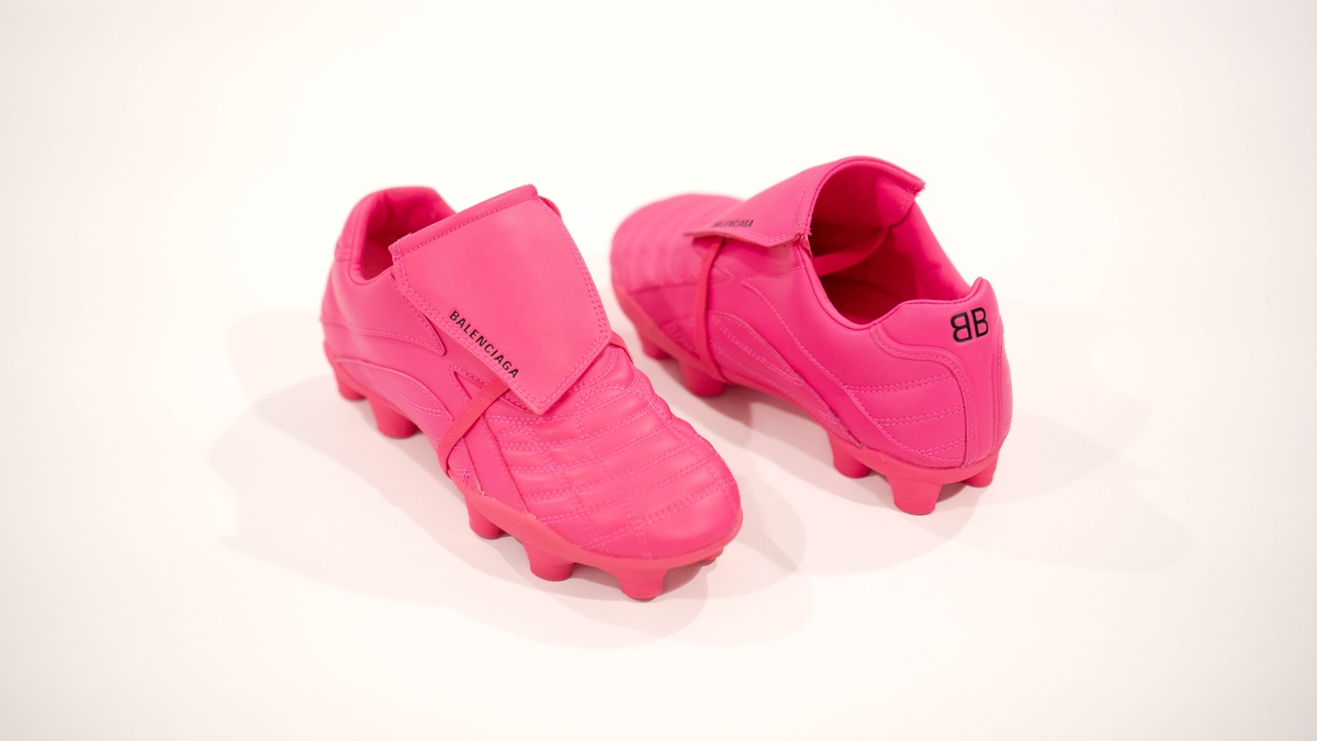 Pink football boots with Velcro straps and embossed Balenciage logo, set against a white background.