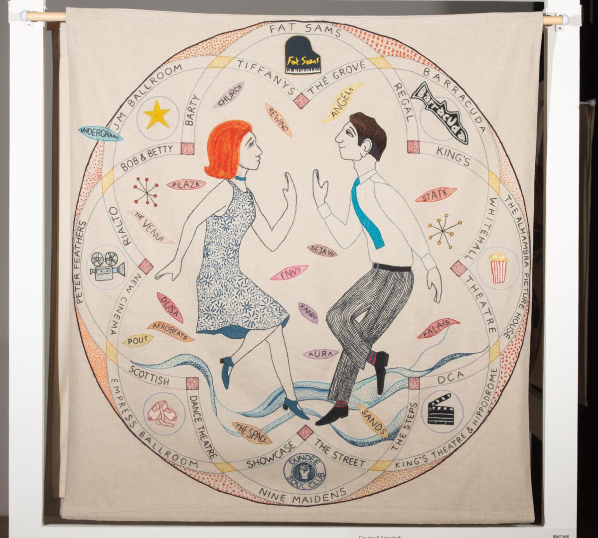 A woven tapestry with bold colours, two people are dancing in the middle