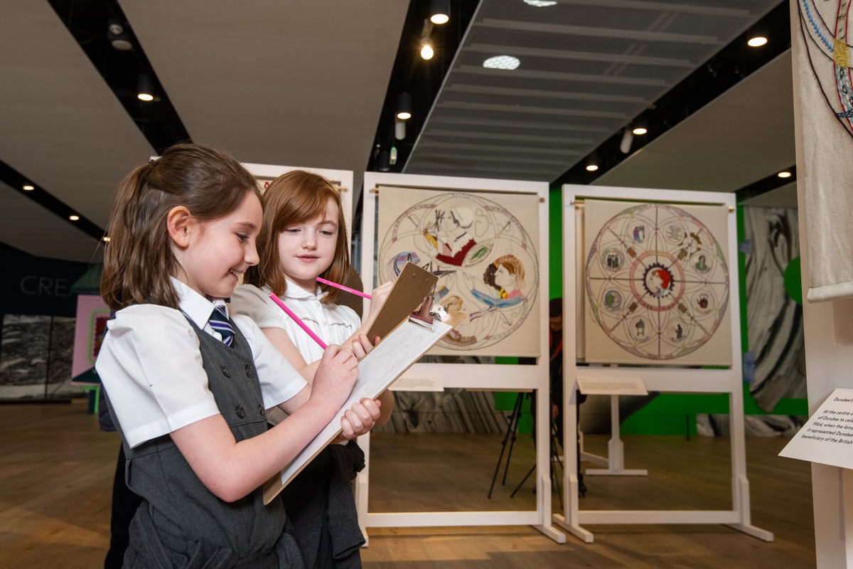 Two small children with clipboards standing next to tapestries