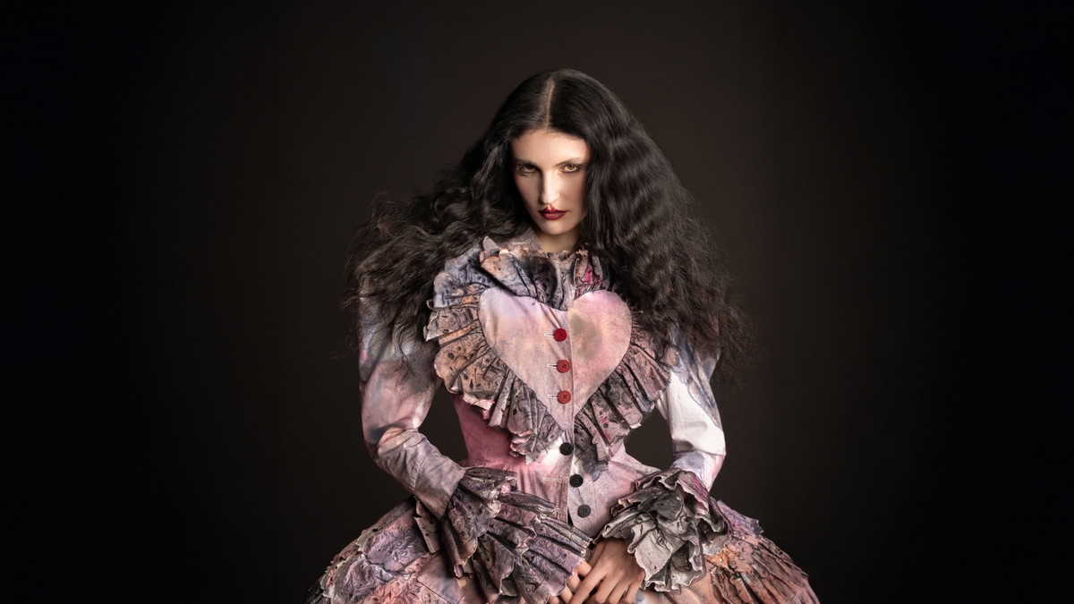 A model wearing a pink dress with a love heart detail against a black background.